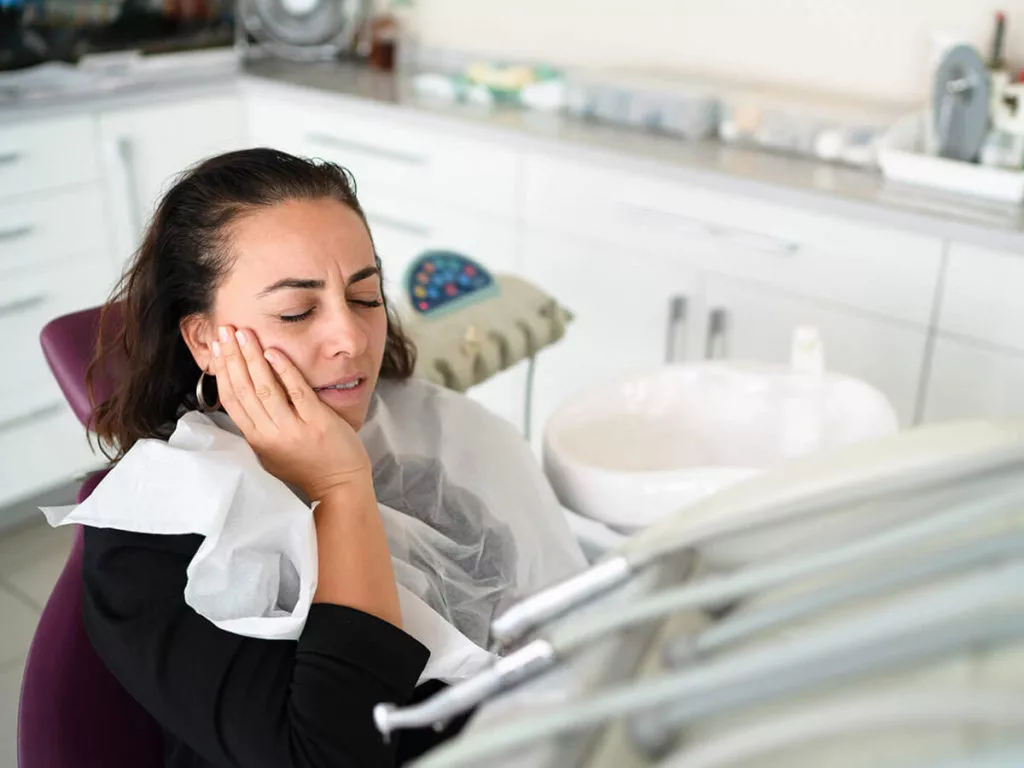 woman sitting in exam chair holding tooth in pain