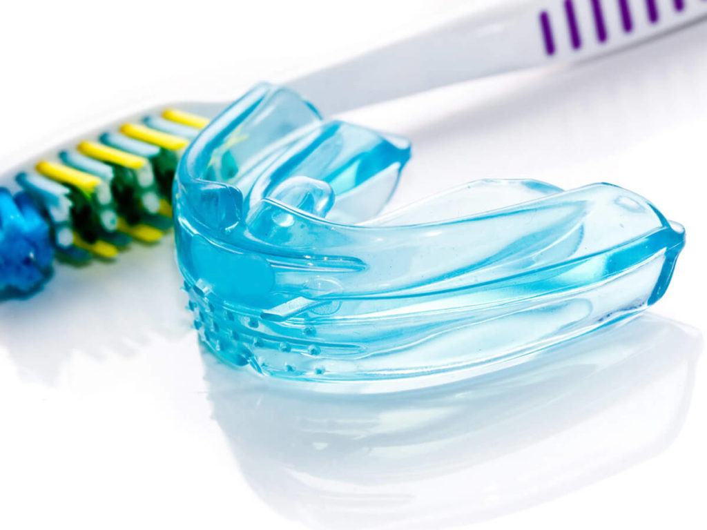 blue, clear mouth guard laying next to tooth brush