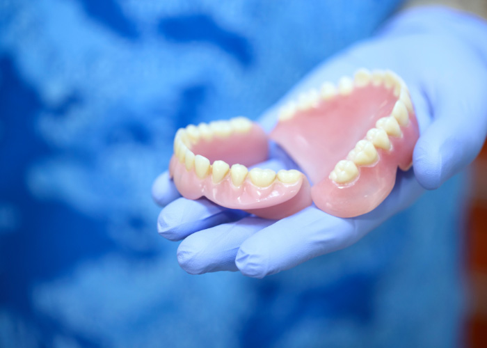 dentist wearing blue gloves holding a top and bottom denture