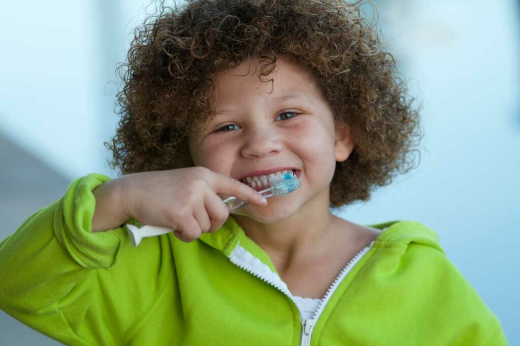 child wearing a green jack smiling and brushing their teeth