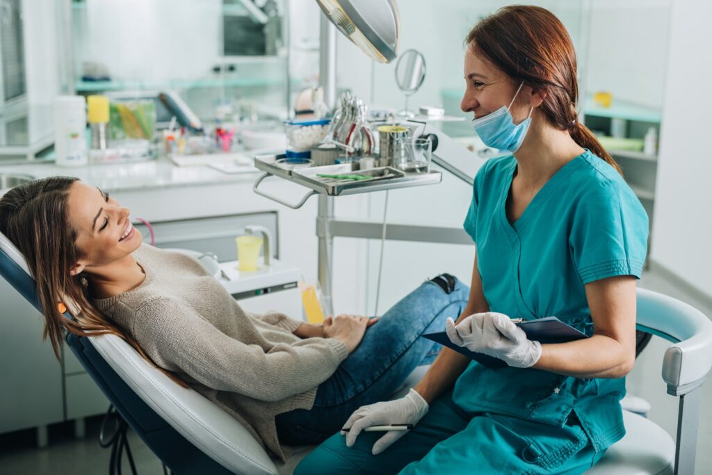dental assistant and patient in exam room looking at each other smiling