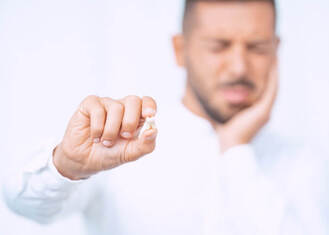 man in a white shirt holding his jaw in pain while holding out a tooth